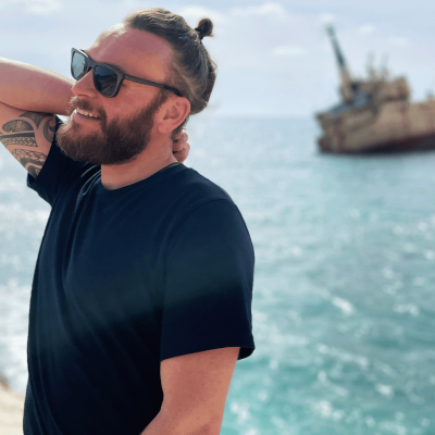 Ein Mann in einem dunklen T-Shirt, der neben dem Meer steht.